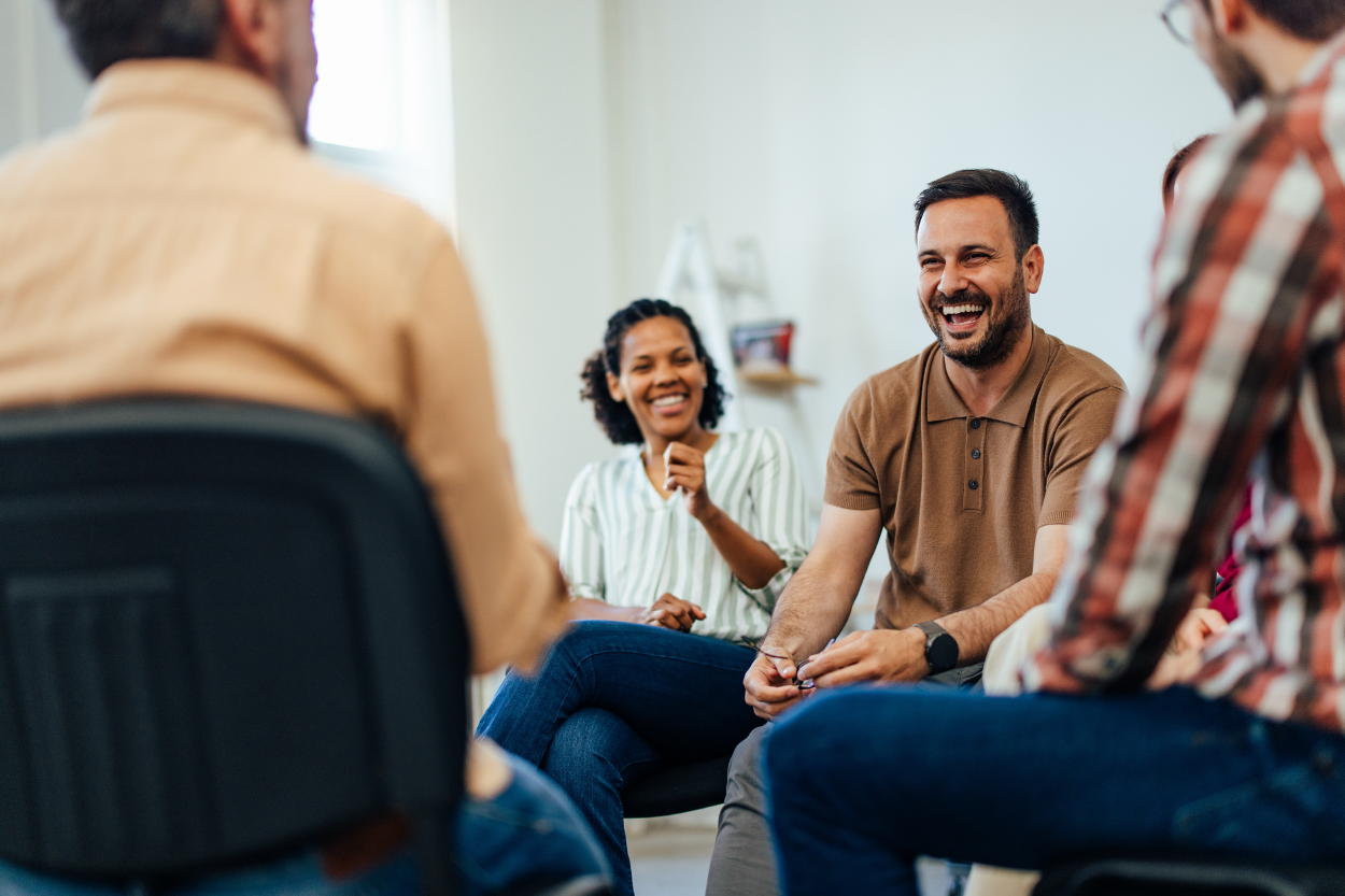 small group sitting in a circle; focuses on a man and woman who are smiling and laughing